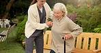 Nurse, helping and senior woman with cane on bench for assisted living in outdoor garden. Female person, caregiver or aid with elderly patient or walking stick for mobility, care or support in park