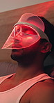 Mask, relax and man with red light therapy on bed for skincare, beauty or facial wellness. Health, cosmetic and person with face LED treatment for collagen production in bedroom at apartment.
