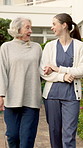 Senior, woman and walking with nurse in outdoor garden for mobility, exercise or bonding together. Elderly, female people or caregiver talking with smile or patient for assisted living or support