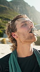 Runner, man and drinking water in nature with break, hydration and training outdoor for fitness. Happy, male person and exercise rest by mountain with beverage, electrolytes and cool down in summer.