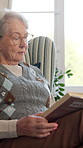 Senior, woman and reading book in house with glasses, relax or retirement hobby for knowledge growth. Calm, elderly person and spectacles in living room with literature, story and novel for wellness.