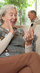 Phone, video call and wave with old woman on sofa in home living room for break or virtual chat. App, conversation and greeting with happy senior in apartment for online or mobile communication