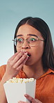 Scared, woman and watching tv in studio with popcorn, horror movie and reaction to crime thriller. Shocked, person and fear with snack for streaming, suspense scene and creepy film on blue background