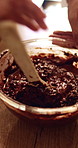 Mix, hands and mother with child for batter in kitchen for baking, dessert or cupcakes in home. Stirring, wooden spoon and mom with kid for teaching with chocolate mixture for cake in apartment.