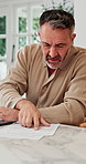 Man, laptop and paperwork in home for finance, budget planning or asset management in kitchen. Mature person, typing or checking invoices with tech for financial expenses and documents in house