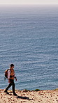 Walking, hiking and man with ocean view on adventure, journey or trip for exploration on vacation. Trekking, holiday or person outdoor by cliff for travel, space or sightseeing with scenery of sea