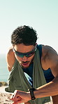 Fitness, break and man by beach with smart watch, track heart rate or earphones for music playlist. Person, sunglasses and exercise rest outdoor by sea with audio tech, timer or wellness notification