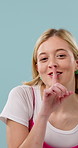 Happy, secret and face of woman in studio with confidential information, news or quiet voice. Smile, whisper and portrait of person with finger on mouth for gossip or silence on blue background.