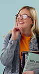 Woman, thinking and college student in studio with books, glasses and idea for science education. Happy, person and learning with university textbook, reflection or biology course on blue background.