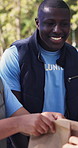 Volunteer, team and man with food donation outdoor, help and poverty relief with outreach program. Happy person, charity and humanitarian aid with meal, talking or non profit with community service