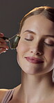 Facial massage, skincare and woman with jade roller, self care or cosmetics with anti aging benefits. Studio background, dermatology and happy person with tool for healthy skin and lymphatic drainage