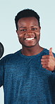 Thumbs up, weights and face of man in studio for exercise, fitness and bodybuilder workout for strength. Happy, portrait and African person with emoji, approve and strong muscles on blue background