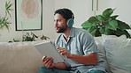 Thinking, tablet or man with headphones in home for playlist, streaming audio or scroll to search song. Tech, music and person in living room, listen to media or podcast decision on internet to relax