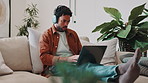 Man, laptop and headphones with typing on sofa for social media, reading blog and streaming service. Networking, email and podcast with person in living room of home for website, sign up and relax