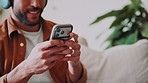 Hands, phone and man with headphones in home for subscription, podcast or streaming audio. Mobile, music and happy person on living room sofa, listen to sound or typing text message on social media
