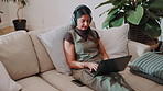 Headphones, typing and laptop with woman on sofa for social media, reading blog and streaming service. Networking, email and search with person in living room of home for website, sign up and relax