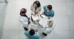 Above, nurse and doctors in meeting with document, patient charts and planning for treatment. People, team and talk in hospital with paperwork, medical records and case study for healthcare services