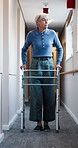 Walking, hallway and senior woman with frame in nursing home for movement, mobility and wellness. Retirement, facility and elderly person with disability, support and balance for recovery in corridor