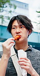 Asian man, eating and outdoor with food for travel, walk and journey with traditional snack. Hungry person, skewer stick or bite in city for for nutrition, cuisine or local meal for wellness in Japan