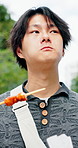 Asian man, food and eating in city with travel, walking and journey with traditional snack. Hungry person, skewer stick or outdoor with bite for nutrition, cuisine or local meal for wellness in Japan