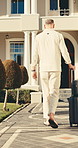 Travel, man and walking with suitcase for hotel arrival, weekend stay and getaway destination. Back, guest and luggage outdoor for solo trip, accommodation entrance and check in for vacation booking