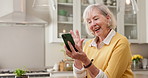 Senior, wave and happy woman with phone for video call, conversation or friendly chat in kitchen. Elderly, female person or hello with smile or discussion for communication or virtual talk in home