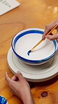 Hands, person and painting for pottery with mold, sculpture and custom design of handmade craft. Potter, paint brush and decoration in workshop with clay bowl, artistic process and porcelain creation