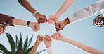People, meeting and friends with fist bump for social cohesion, collaboration or mission in unity. Low angle, group or community with hands together or blue sky for synergy, teamwork or support