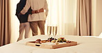 Hotel bed, champagne and couple with breakfast tray, anniversary celebration or luxury travel. Room service, hug and people with sparkling wine for romantic getaway, fruits and hospitality pastries