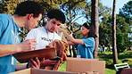 Volunteer, team and packing boxes in outdoor park for donation checklist or charity organization. Group, people or NGO with clothing, packages or clipboard for community service or outreach in nature
